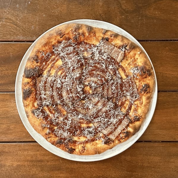 Miko's Calitalia pizza with a spiral of sauce, meat, and grated cheese on a wooden table.
