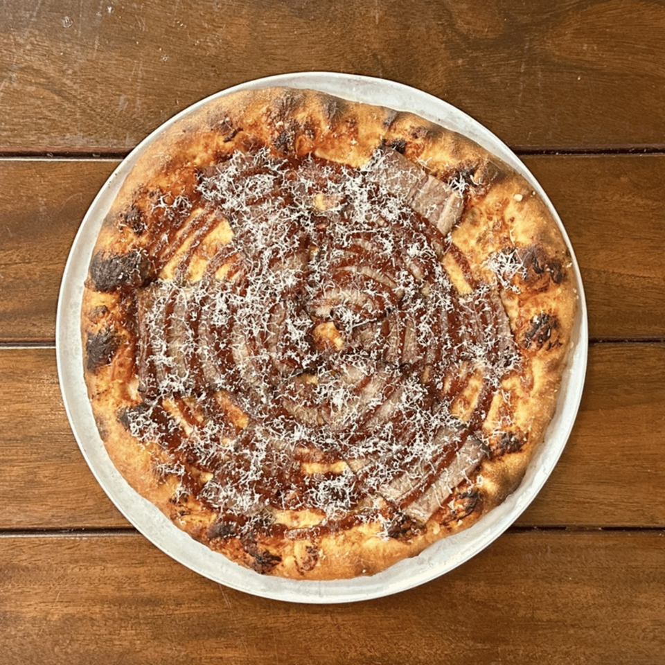 Miko's Calitalia pizza with a spiral of sauce, meat, and grated cheese on a wooden table.