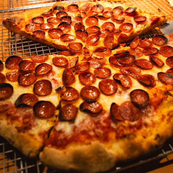 Two slices of Miko's Calitalia pepperoni pizza with melted cheese on a cooling rack.